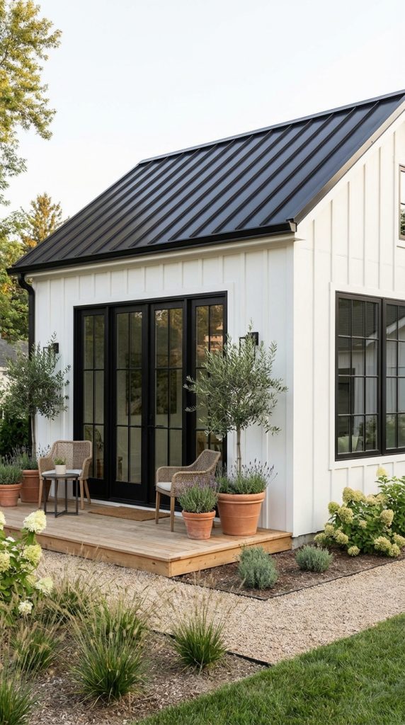 Modern farmhouse she shed idea with white board and batten siding, black French doors, metal roof, and small wood deck.