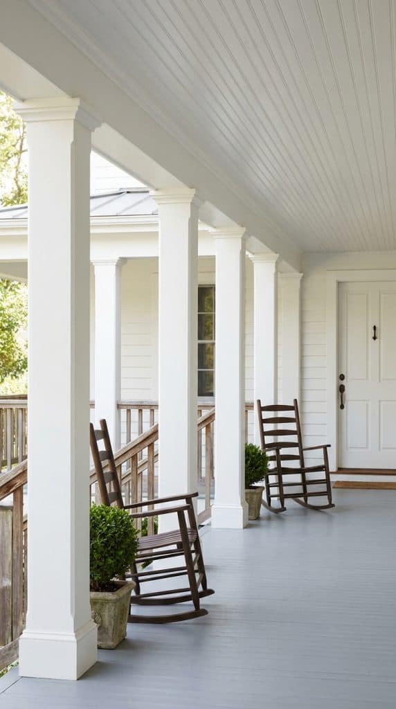 Square white farmhouse porch columns aligned along a covered porch with beadboard ceiling and wooden rocking chairs.
